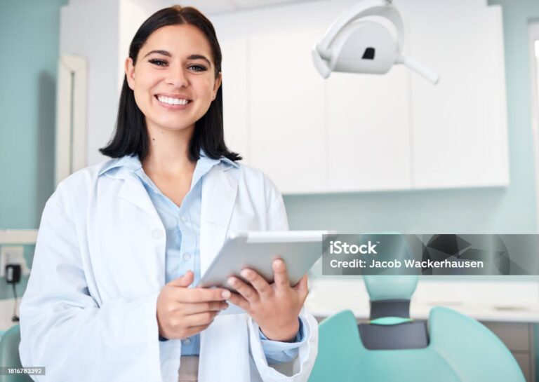 Young female caucasian dentist wearing a labcoat and smiling while using a digital tablet in her office. Dental hygiene is important to your wellbeing